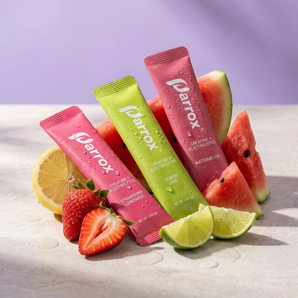 Three Narrox electrolyte stick packets in pink, green, and magenta are arranged on a light stone surface with sliced strawberries, watermelon, lime, and lemon around them against a soft lavender background.